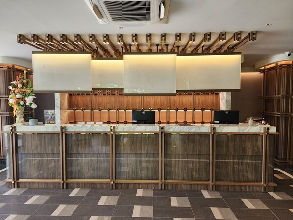 A modern hotel reception area with a marble counter, wooden paneling, and a large floral arrangement.