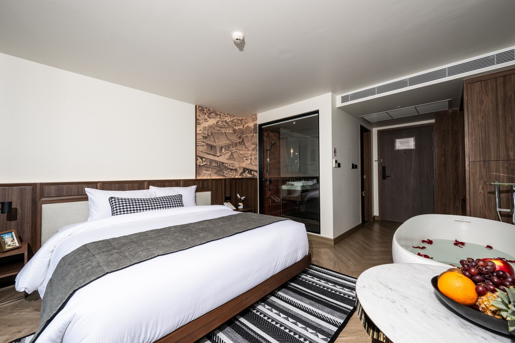 Una habitación de hotel moderna con una cama grande, un baño con bañera y un comedor con frutero.