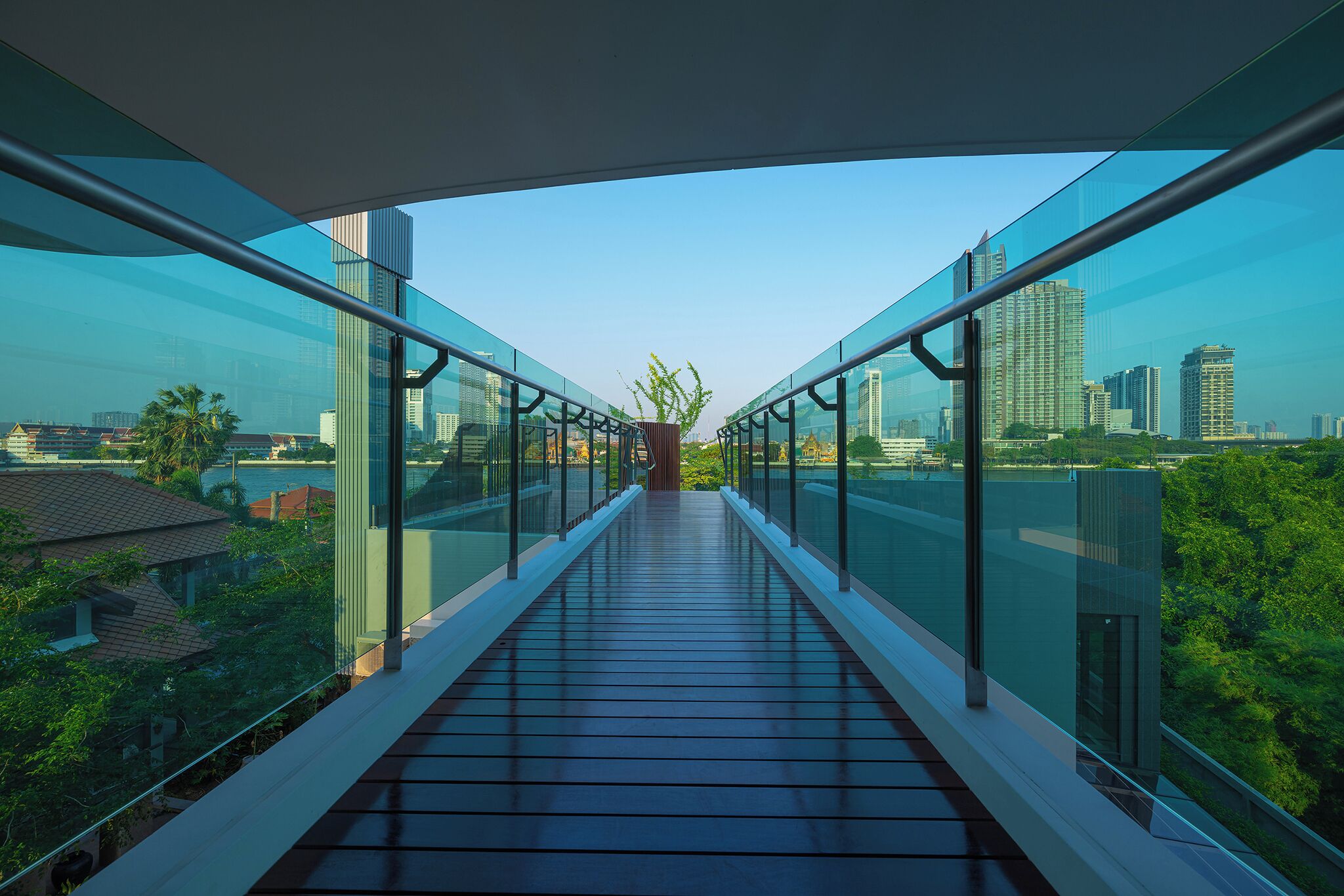 Eine moderne Glasbrücke mit freiem Blick auf die Stadtlandschaft und die darunterliegende Grünfläche.