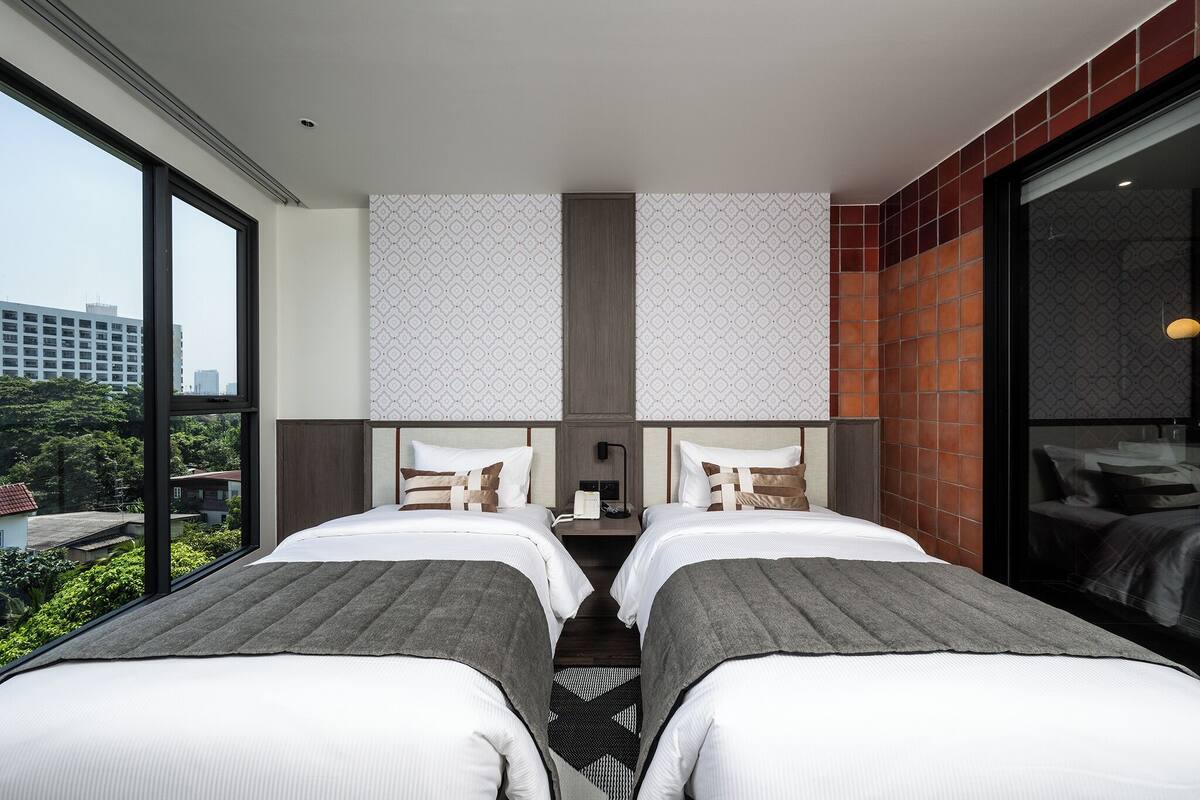 Quarto de hotel com duas camas, uma janela grande e vista para a cidade.
