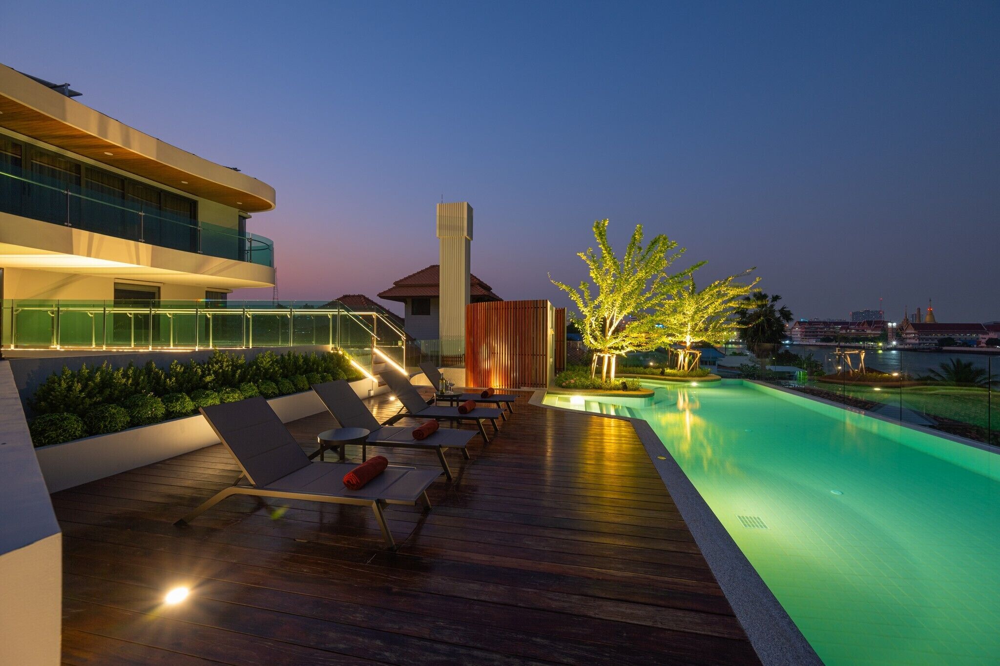 Un área de piscina en la azotea con sillones de descanso y una piscina, rodeada de edificios modernos y un paisaje urbano al fondo.