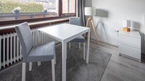 A modern room with a white table and two grey chairs, a floor lamp, and a white cabinet. - Apartment Meeresbrise, Modern & Liebevoll Eingerichtet, Wlan, Smart TV (Wilhelmshaven)