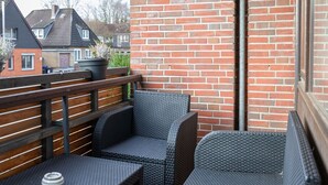 A balcony with wicker furniture, a potted plant, and a view of neighboring houses. - Apartment Meeresbrise, Modern & Liebevoll Eingerichtet, Wlan, Smart TV (Wilhelmshaven)