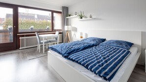 A modern bedroom with a large bed, a desk, and a view of the outside. - Apartment Meeresbrise, Modern & Liebevoll Eingerichtet, Wlan, Smart TV (Wilhelmshaven)