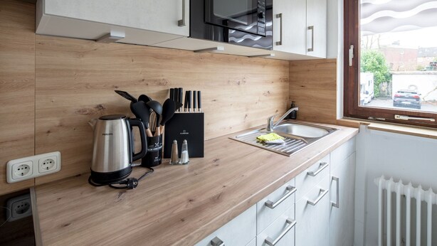 A modern kitchen with wooden countertops, a built-in microwave, and a window with a view of the street. - Apartment Meeresbrise, Modern & Liebevoll Eingerichtet, Wlan, Smart TV (Wilhelmshaven)