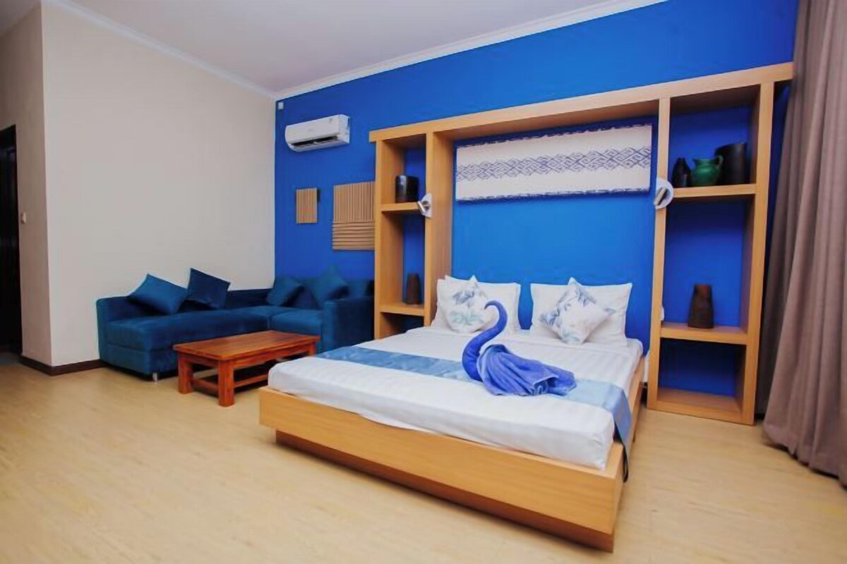 Un dormitorio con cama, un sofá azul, una mesa de centro de madera y un armario con estantes.