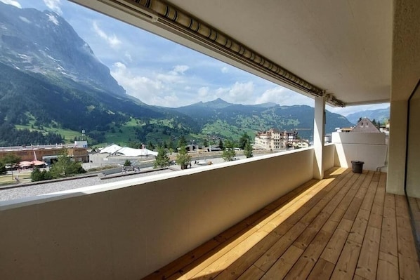A balcony with a wooden floor and a view of a mountainous landscape, buildings, and a road.