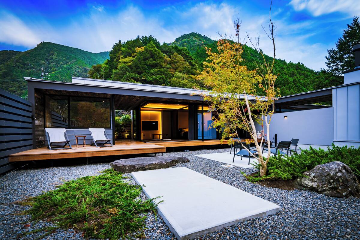 Une maison moderne dotée d’une terrasse, d’un espace salon extérieur et offrant une vue sur une montagne boisée.