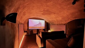 Una sala de cine acogedora, con luz tenue, una pantalla grande, asientos cómodos y un techo abovedado peculiar.
