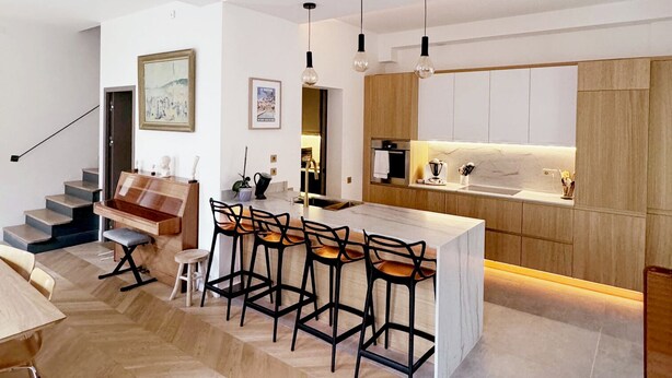 Una cocina moderna con una isla central, taburetes de bar e iluminación colgante.