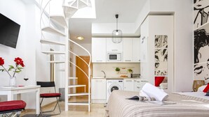 Habitación de hotel compacta con cama, escritorio, silla, kitchenette pequeña y una escalera de caracol.