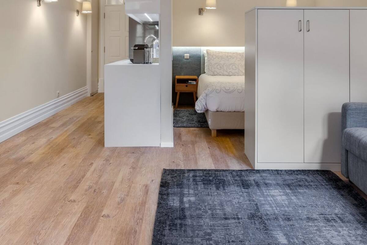 Une chambre compacte comprenant un lit, une armoire, un petit coin cuisine et un canapé gris.
