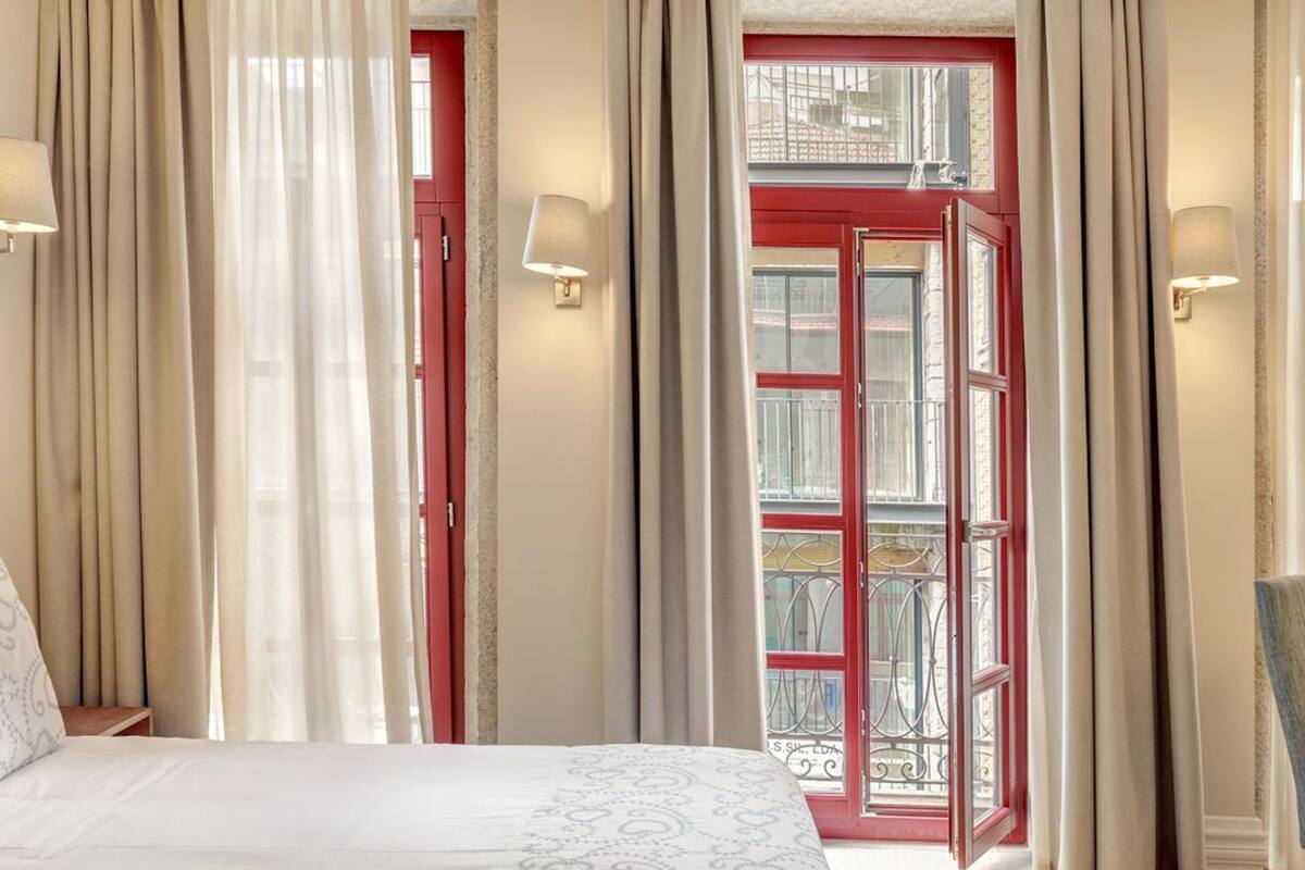 Une chambre d’hôtel avec un lit, des rideaux, une fenêtre et une porte donnant sur un balcon extérieur.