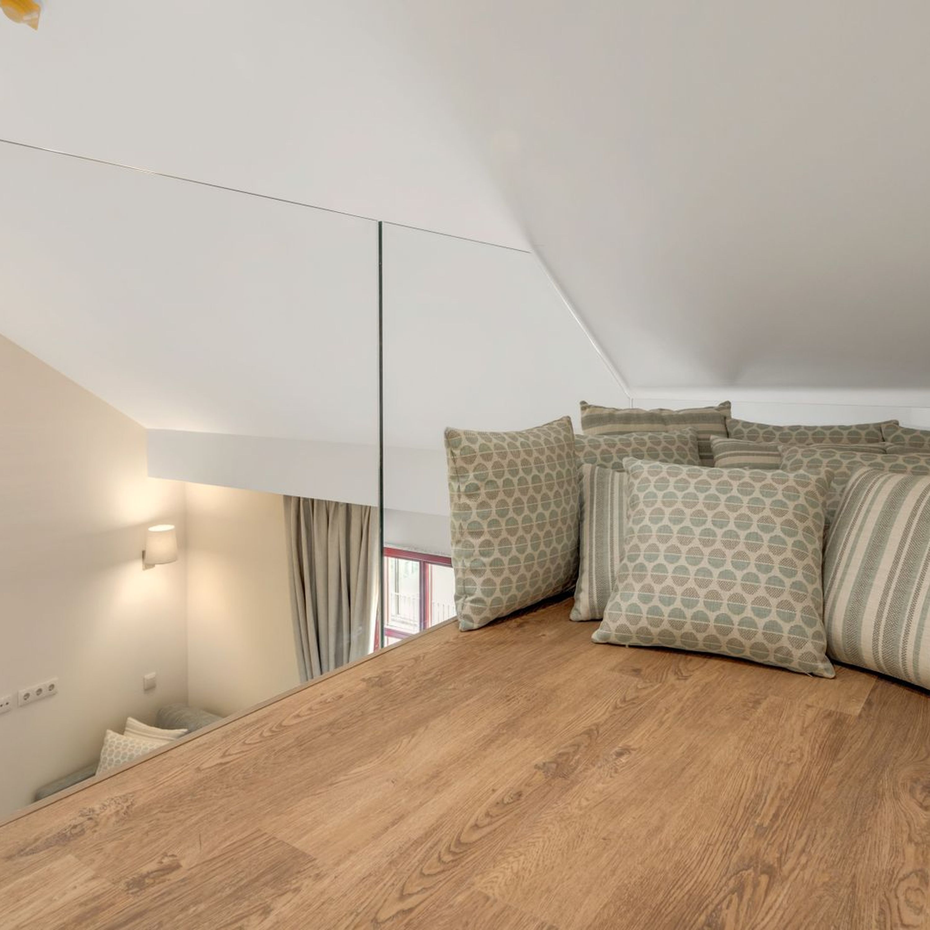 Ett modernt sovrum i loftstil med ett sluttande tak, trägolv och en stor spegel.