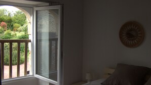 Een slaapkamer met een groot raam, een bed, een nachtkastje en een wandklok.