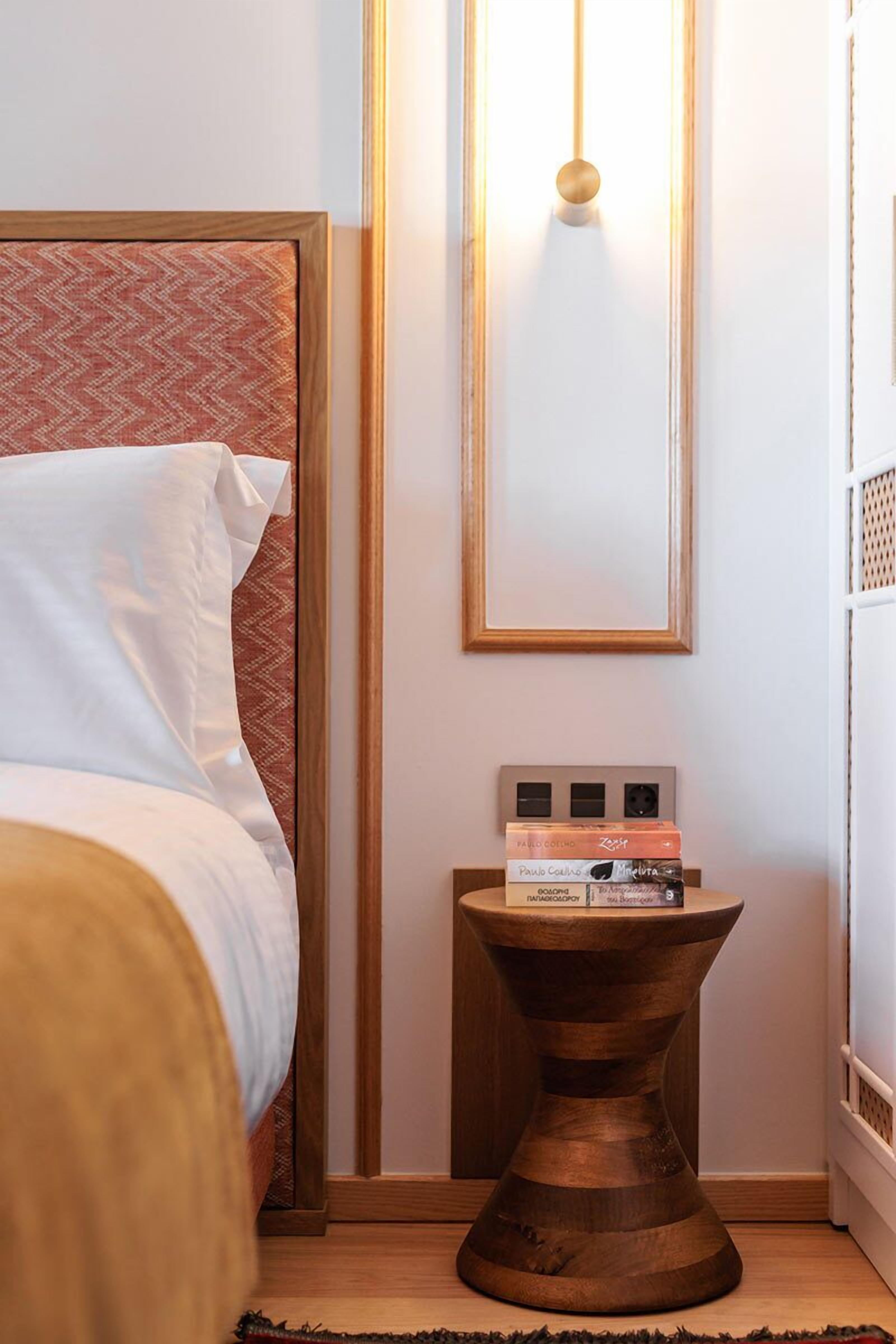 A neatly made bed with white linens, a wooden bedside table with books, and a wall-mounted light fixture.