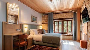 Une chambre confortable avec un lit, un bureau et une chaise, un mur en pierre et une fenêtre avec des rideaux.