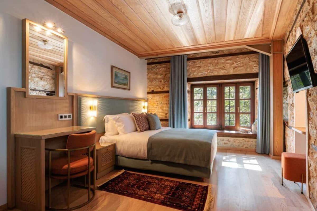 Un dormitorio acogedor con cama, escritorio y silla, una pared de piedra y una ventana con cortinas.