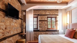 Une chambre avec des murs en pierre, un grand lit, un téléviseur fixé au mur et une fenêtre avec des rideaux.