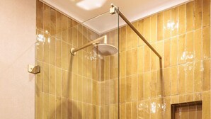 Une douche fermée par des parois en verre, dotée d’un pommeau de douche à main et de commandes fixées au mur.