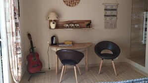Et lille rum med et træbord, to sorte stole, en guitar, en lampe og dekorative genstande på hylder.