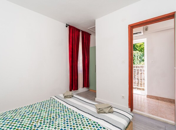 Un dormitorio con una cama, una puerta que da a un balcón y una ventana con cortinas rojas.