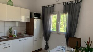 A compact kitchen with a microwave, a sink, and a dining area with a table set for two. - Apartments Rio (Biograd na Moru)