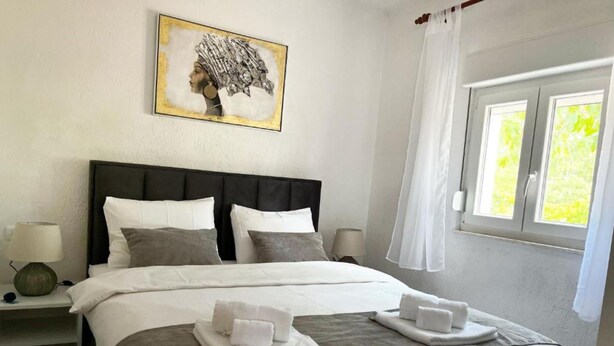 A neatly made bed with white and gray bedding, two bedside lamps, a framed artwork above the bed, and a window with white curtains. - Apartments Rio (Biograd na Moru)