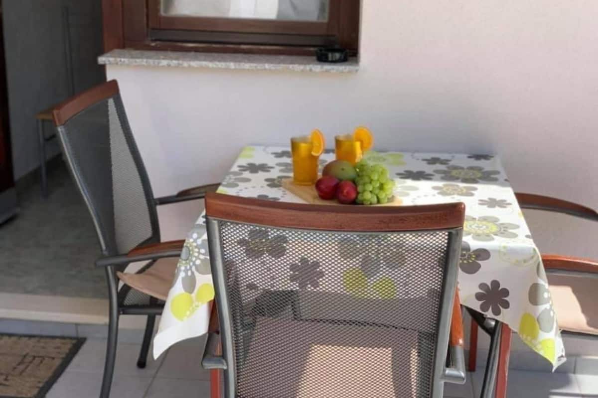 A dining area with a table set for two, a chair, and a window with a view.