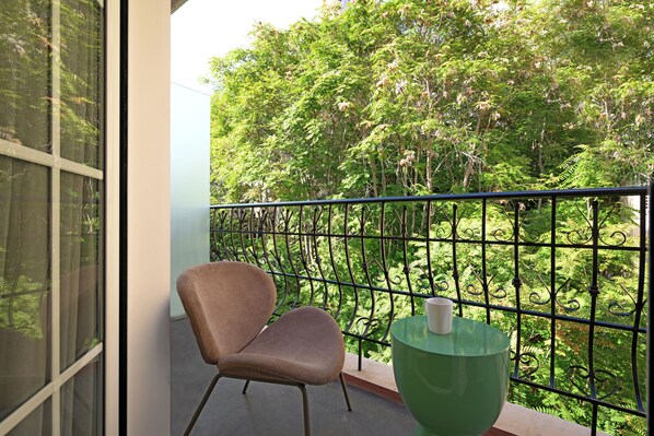 A balcony with a chair and a table, surrounded by a metal railing and lush greenery. - COMFY APART HOTEL (Beirut)