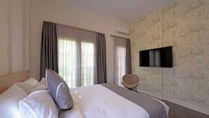 Hotellihuone, jossa on suuri sänky, seinälle asennettu taulutelevisio ja ikkuna, jossa on verhot.