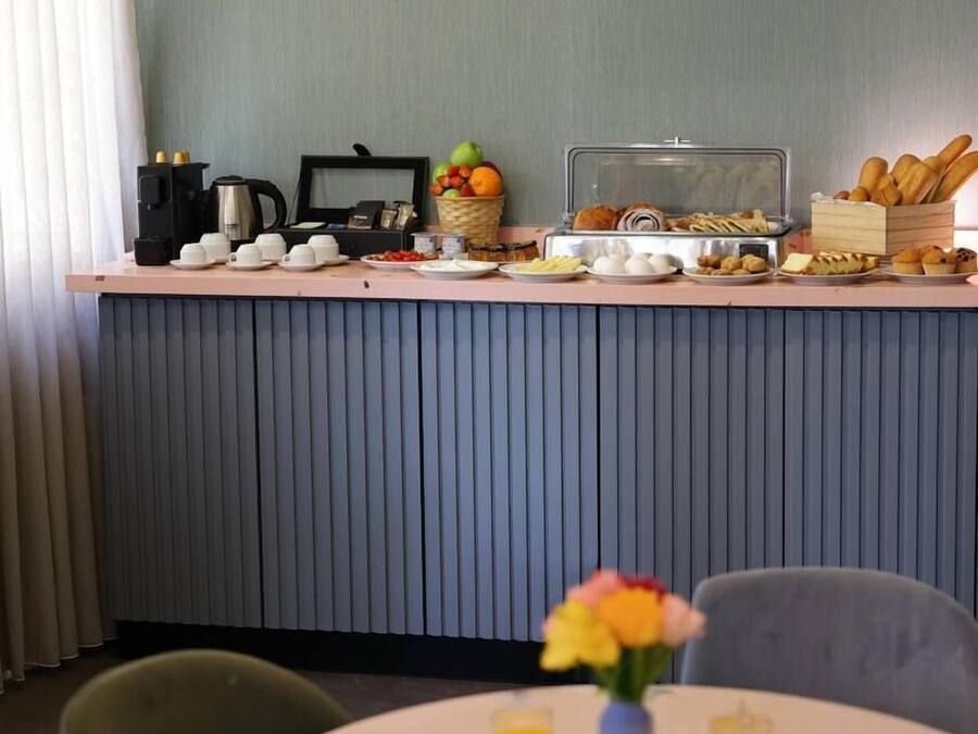 Ein Frühstücksbereich mit einer Theke, auf der verschiedene Speisen präsentiert werden, sowie ein Tisch mit Frühstückstellern, Tassen und einer Blumenvase.