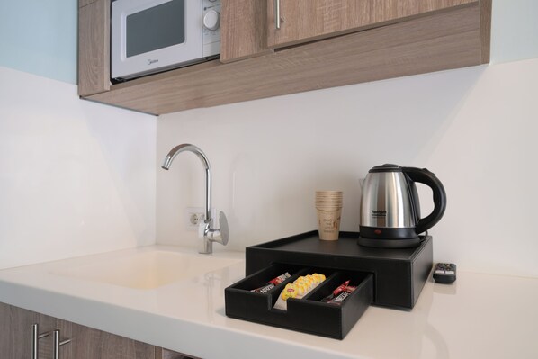 A modern kitchen with a microwave, kettle, and a tray with packaged food. - COMFY APART HOTEL (Beirut)