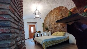 A bedroom with a brick wall, a bed with a patterned bedspread, a hanging light fixture, and a small table with a plant. - Apartamento Turistico Arco Jerez Zafra (Zafra)