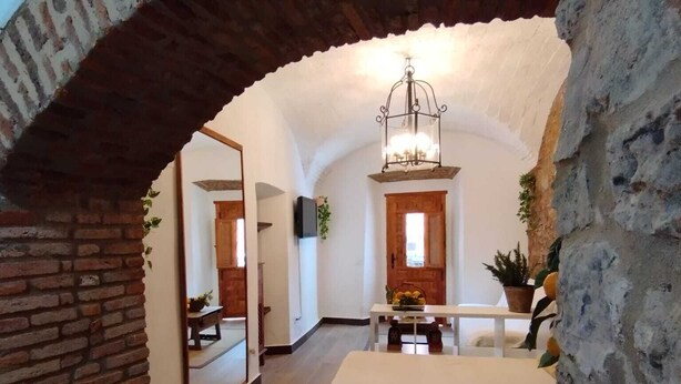 An interior with a brick archway leading to a dining area with a chandelier, wooden table, and potted plants. - Apartamento Turistico Arco Jerez Zafra (Zafra)