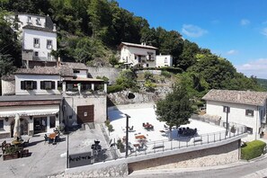 Ein Innenhof mit Außenbestuhlung, Steinbauten und einer Hügelkulisse im Hintergrund.