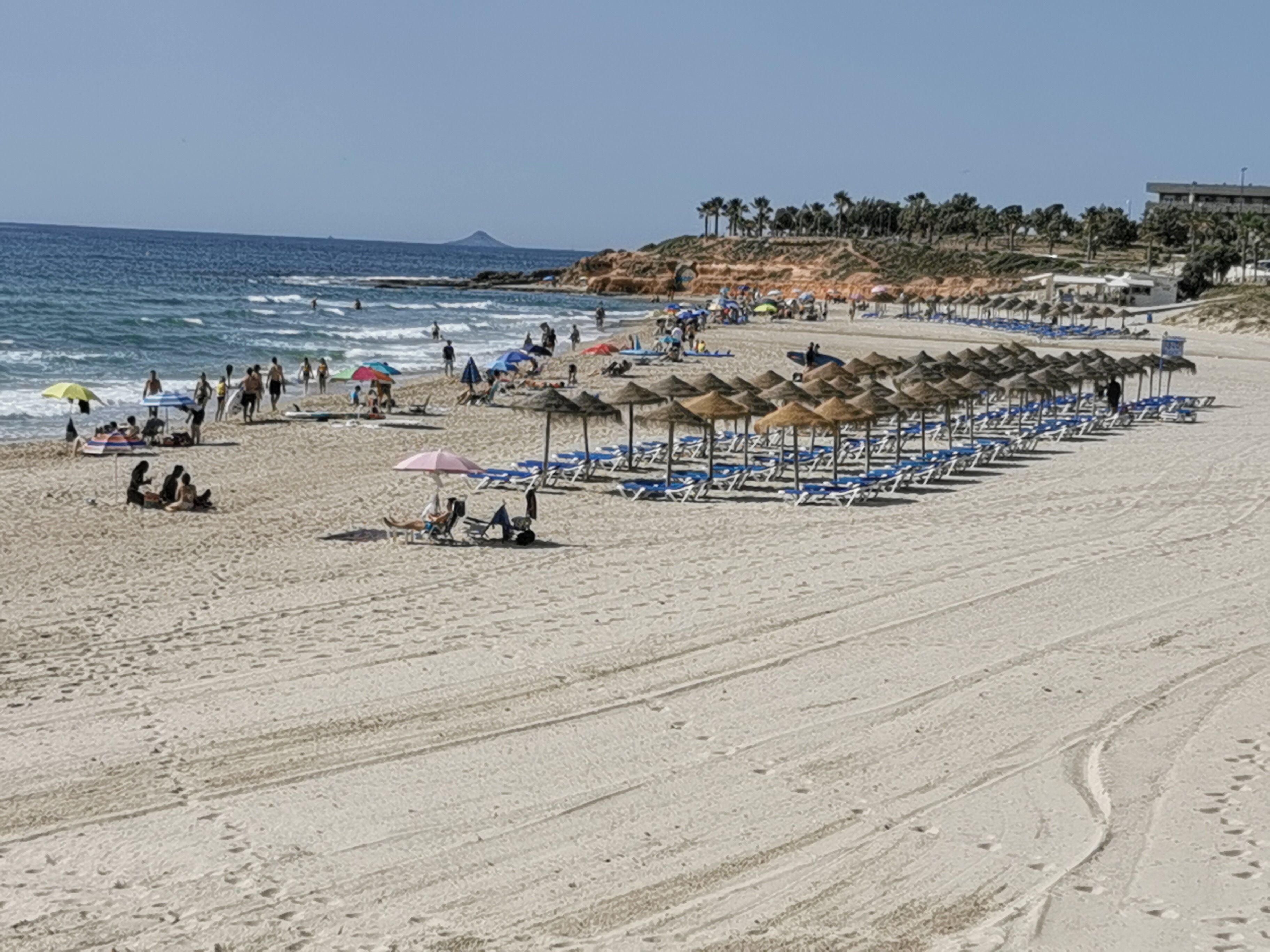 Een strand met rijen parasols en ligstoelen, een zandstrand en de oceaan op de achtergrond.