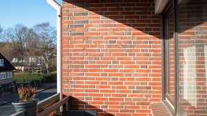 A balcony with a brick wall, two wicker chairs, and a wooden railing. - Ferienwohnung Flut, Modern & Liebevoll Eingerichtet, Wlan, Smart TV (Wilhelmshaven)