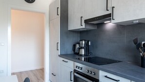 A modern kitchen with grey cabinets, a black stove, and a coffee maker. - Ferienwohnung Flut, Modern & Liebevoll Eingerichtet, Wlan, Smart TV (Wilhelmshaven)