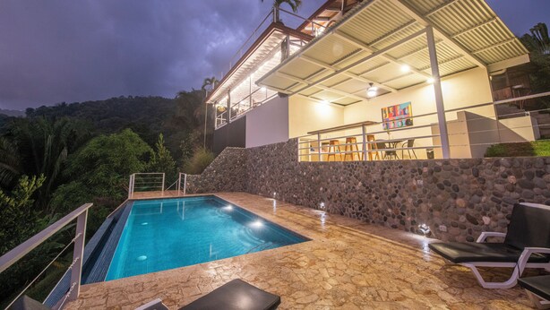 Une piscine avec une terrasse en pierre, un patio couvert et une vue sur un paysage montagneux.