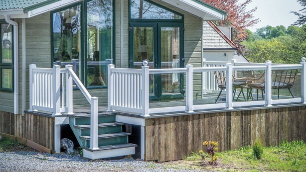 Une maison en bois avec un porche couvert, un escalier menant à une terrasse et des sièges d’extérieur.