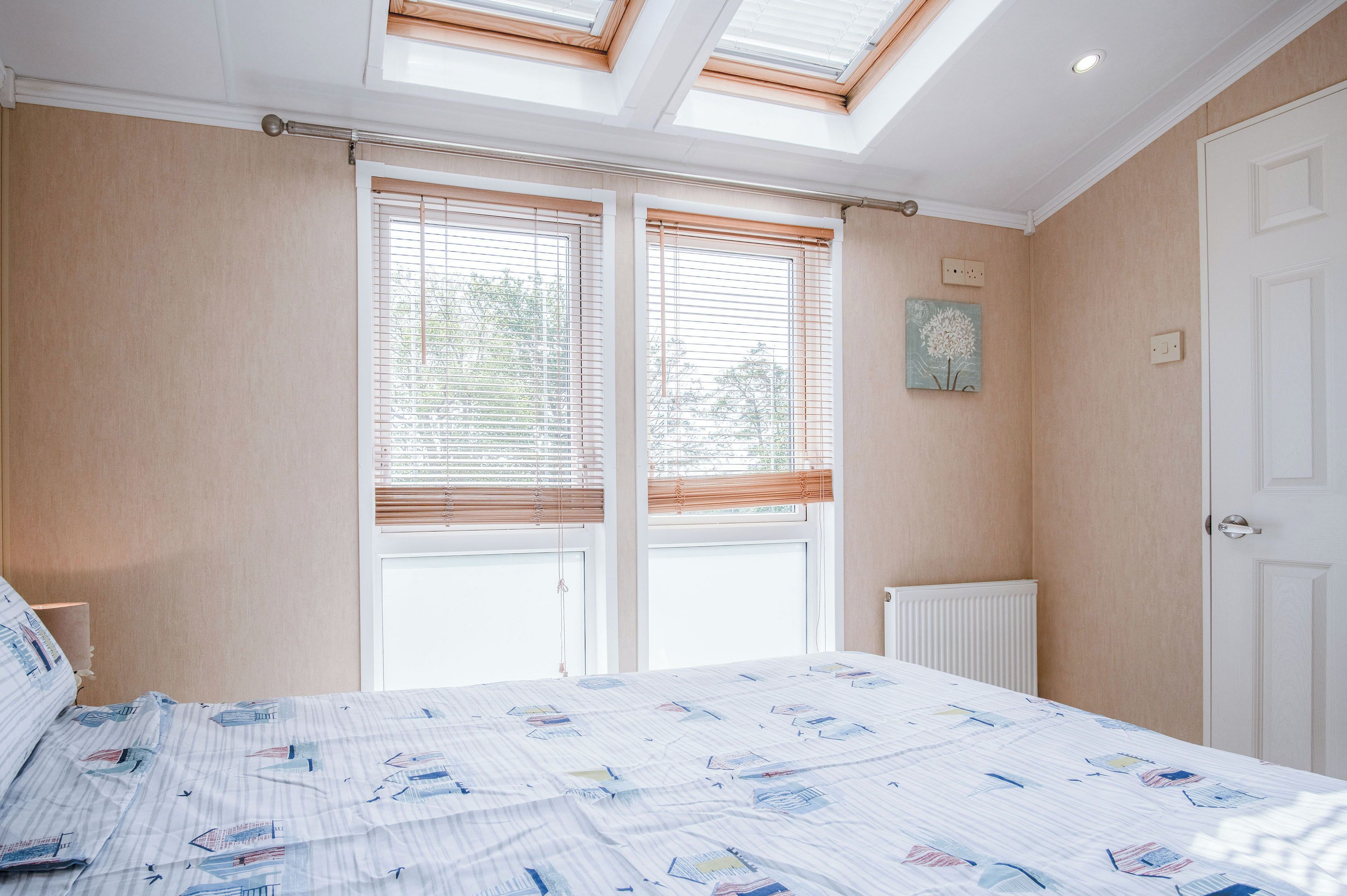 Une chambre à coucher avec un lit, deux fenêtres équipées de stores, un radiateur et une porte.