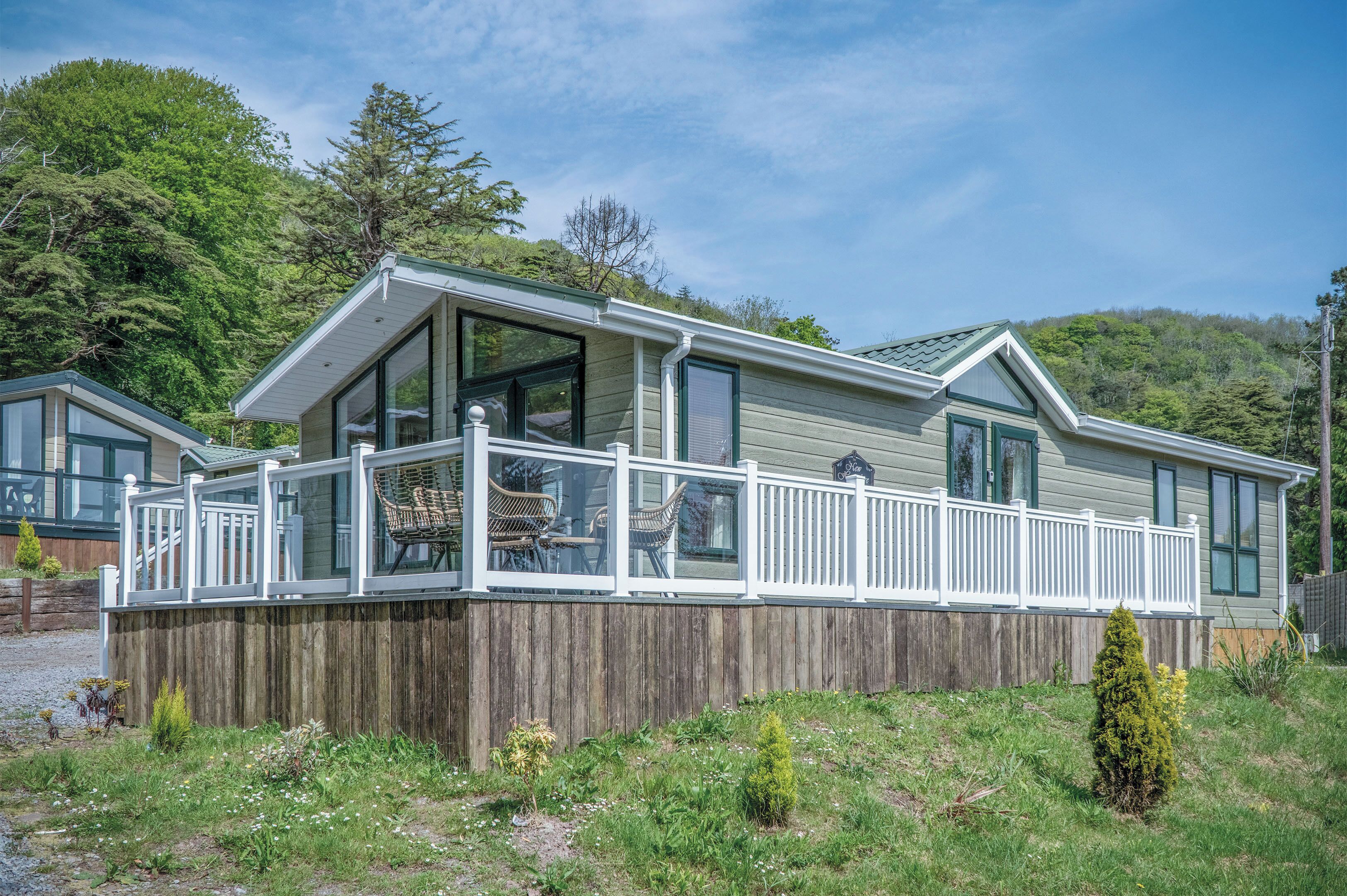 A mobile home with a deck, large windows, and a wooden fence.