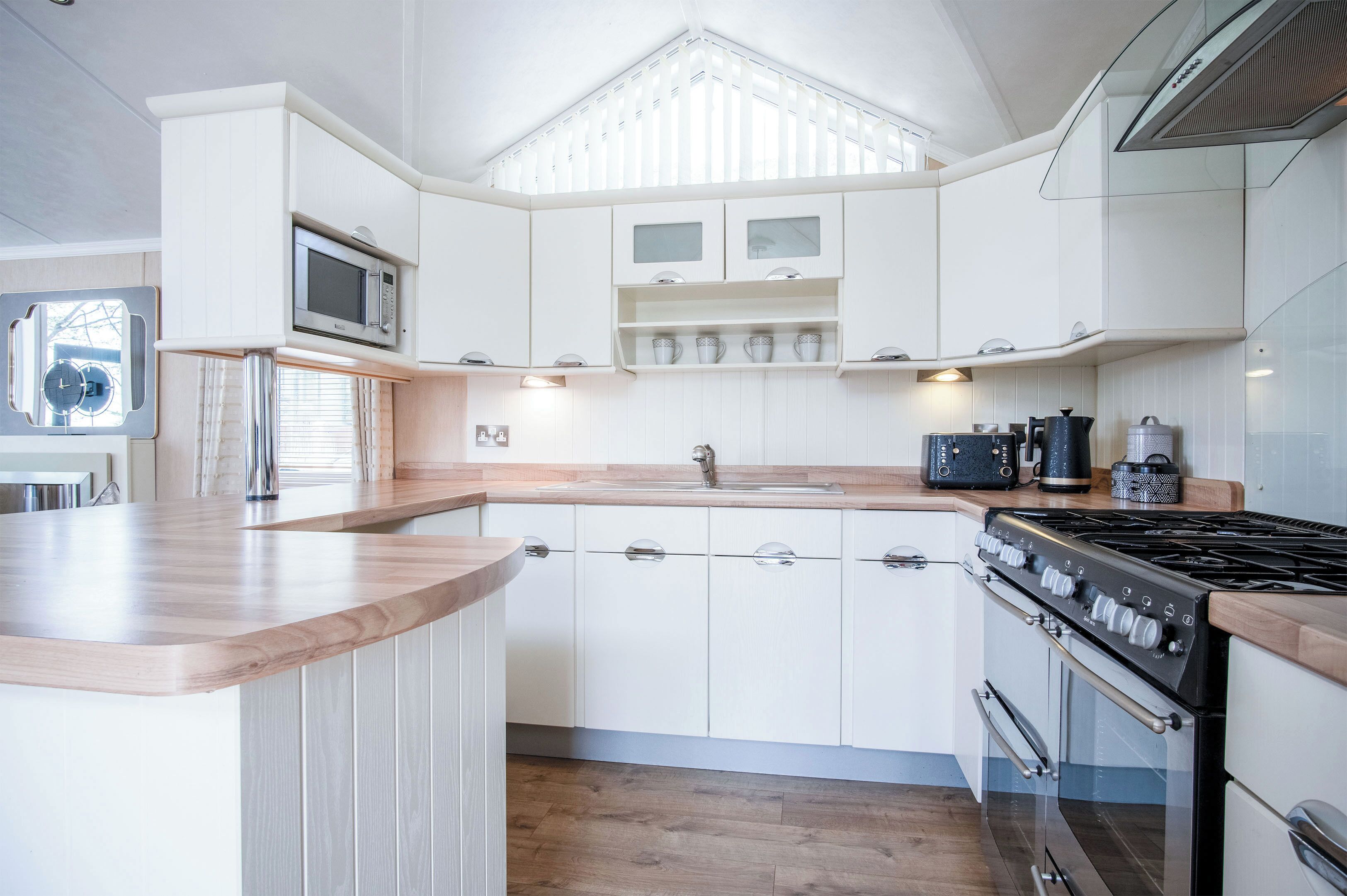 A modern kitchen with white cabinetry, a built-in microwave, a stove, and a sink.