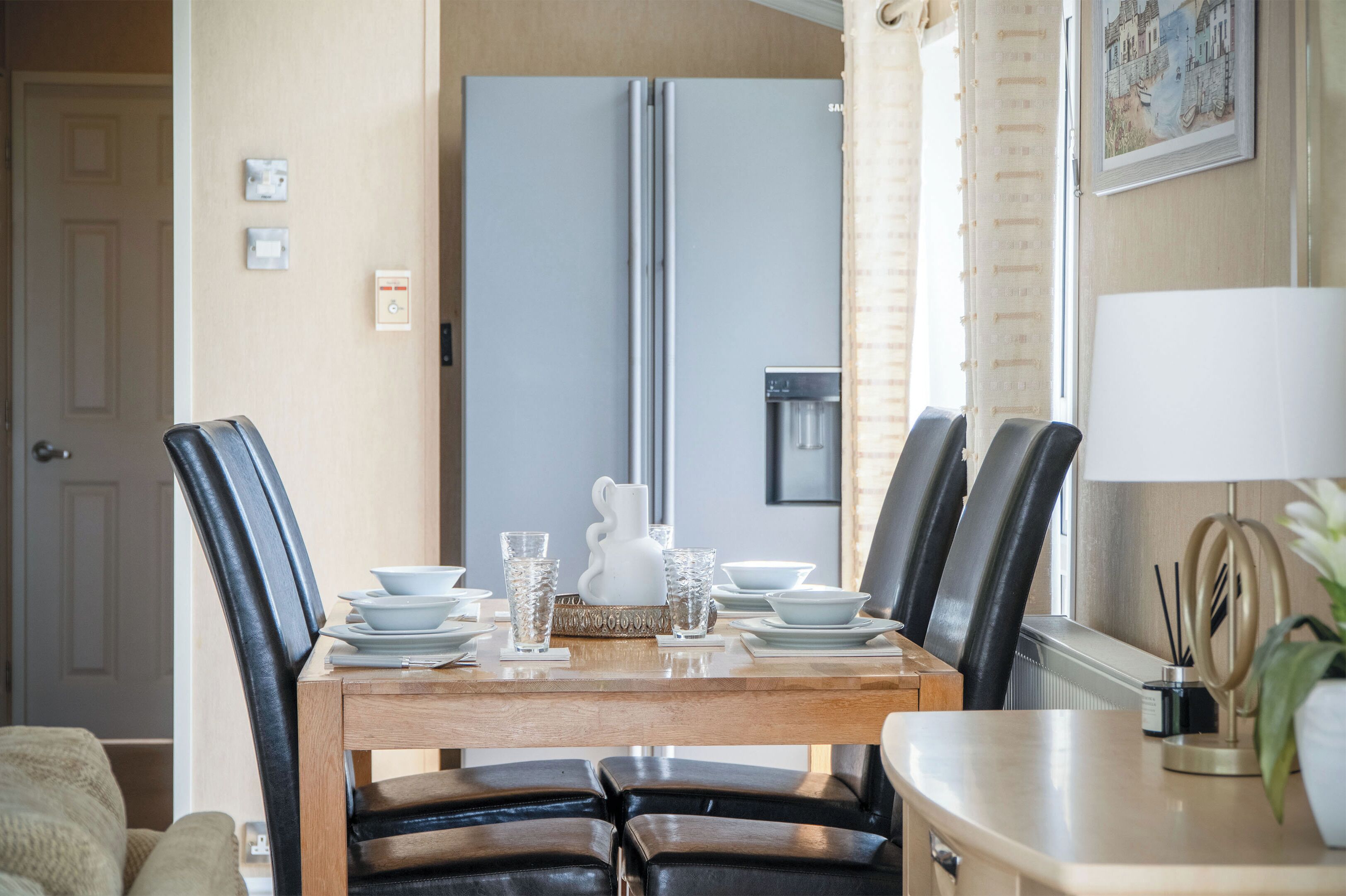 A dining area with a wooden table, black chairs, and a refrigerator in the background.