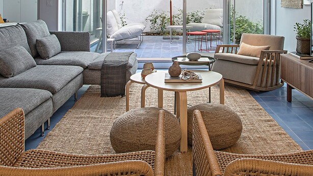 A modern living room with a grey sofa, wicker chairs, a small round table, and a balcony with a red chair and umbrella. - Piso Azul (Lisbon)