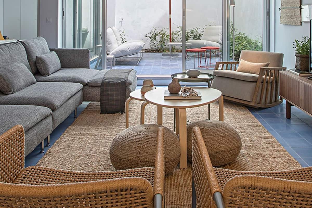 A modern living room with a grey sofa, wicker chairs, a small round table, and a balcony with a red chair and umbrella.