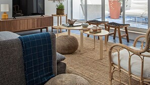 A modern living room with a sofa, coffee table, and chairs, a TV, and a large sliding glass door leading to an outdoor area. - Piso Azul (Lisbon)