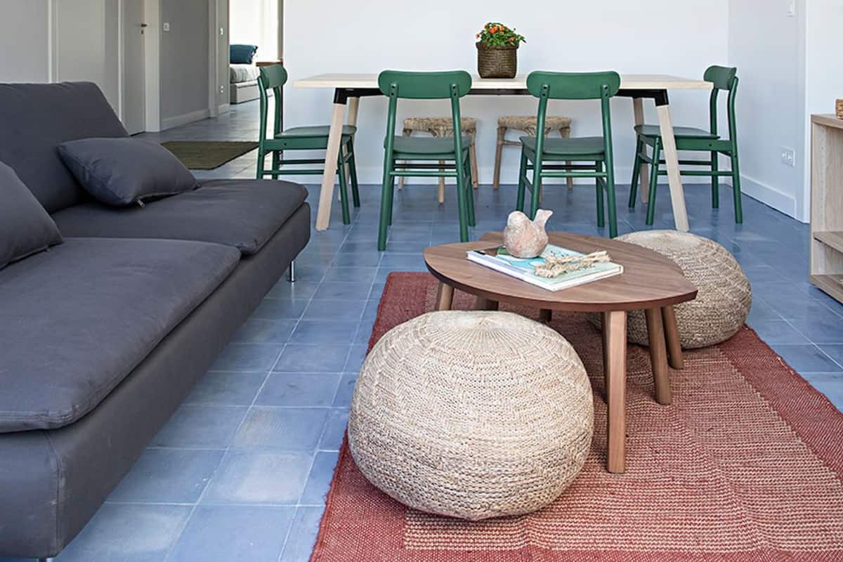 A modern living room with a grey sofa, green chairs, a wooden table, and a woven pouf.