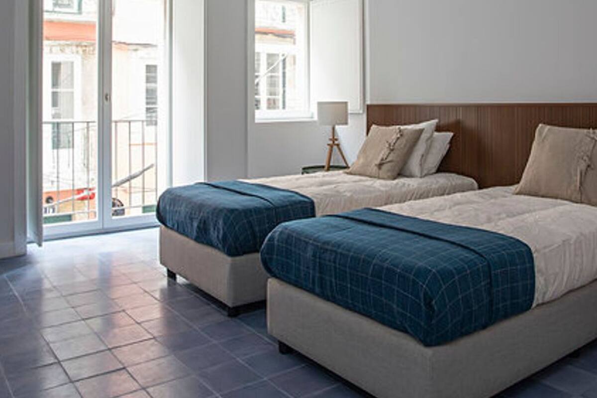 A hotel room with two beds, a balcony, and a view of buildings outside.
